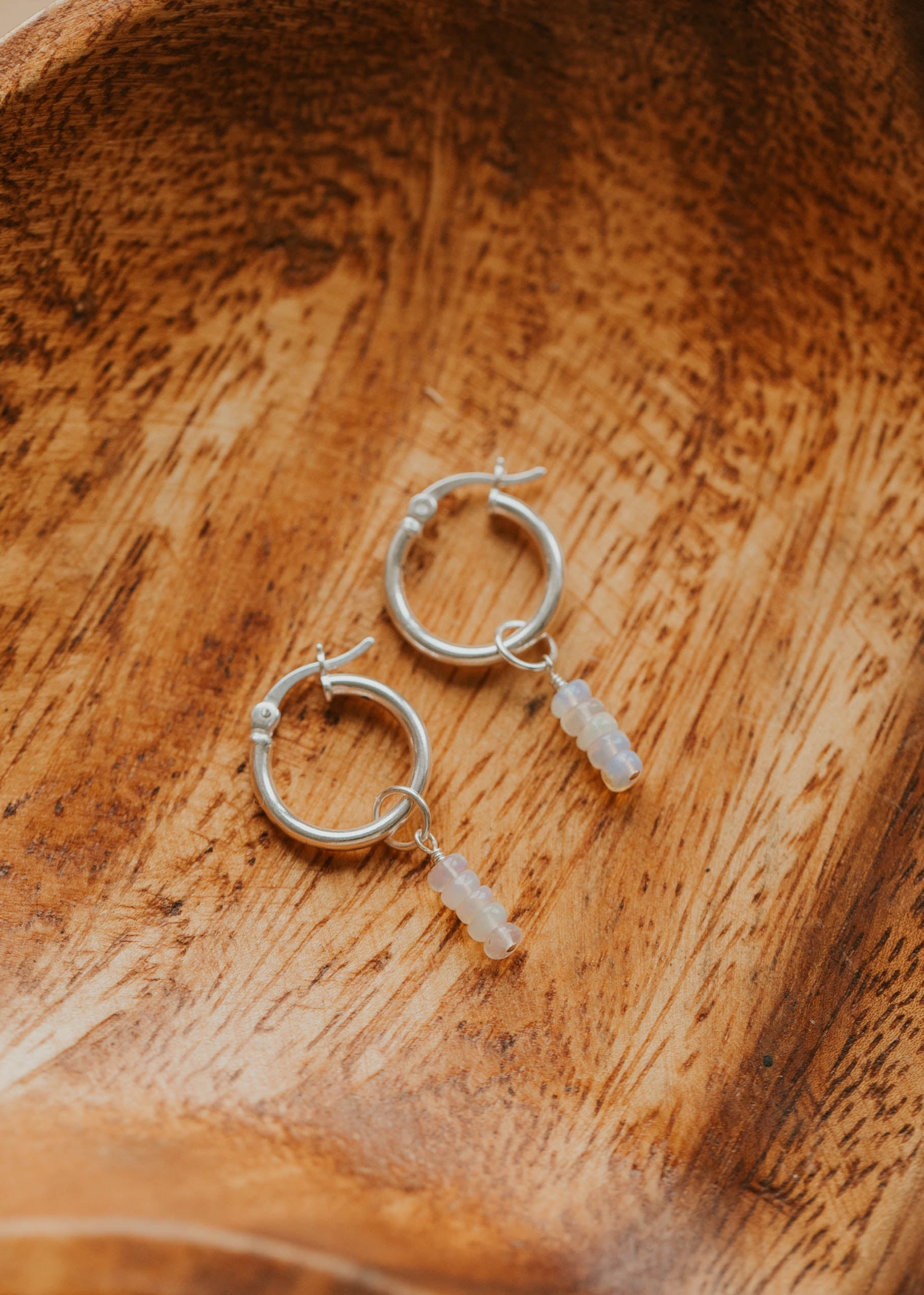 Silver hoop earrings with small stone charms on a wooden surface